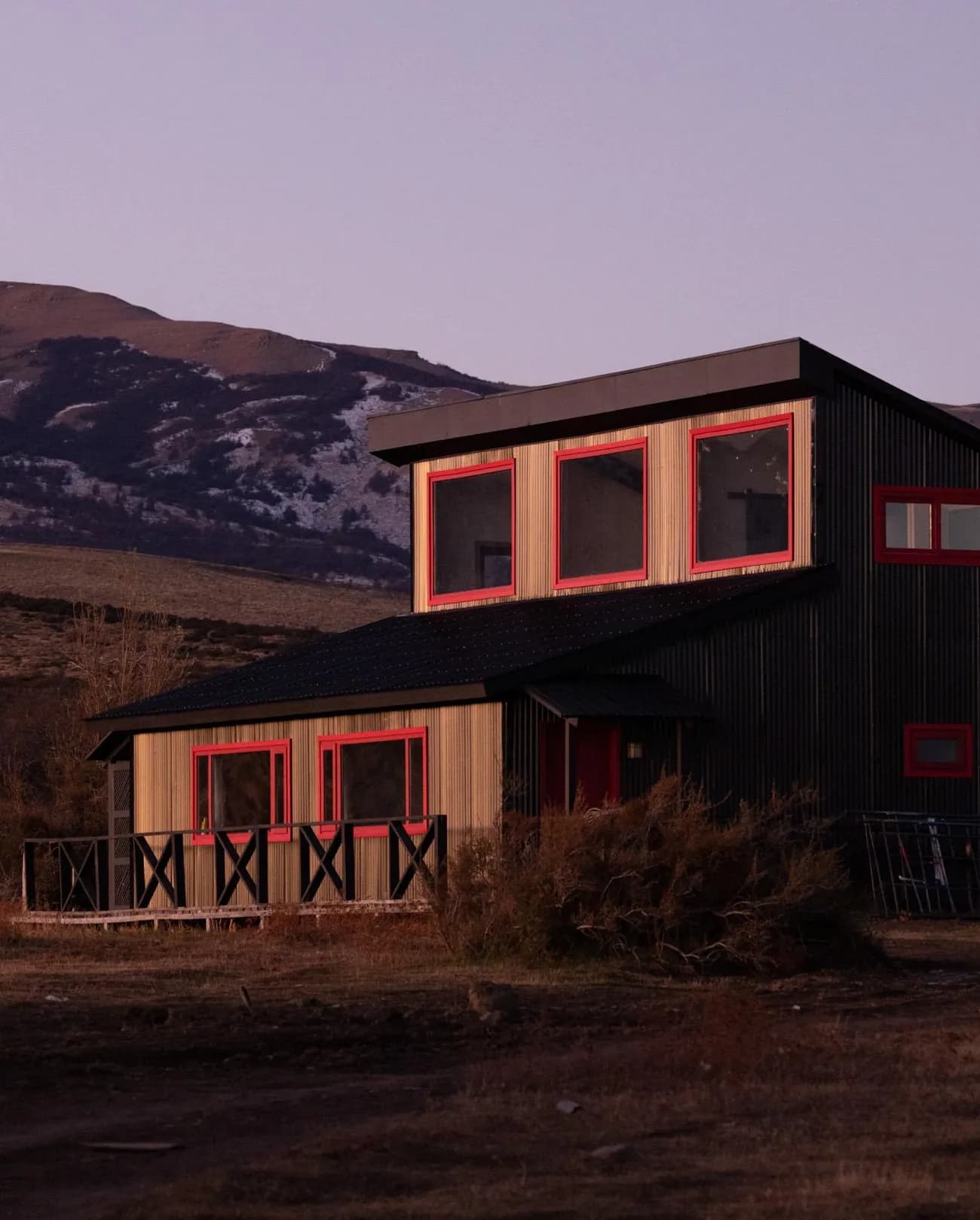 The stable at dusk, a dark timber building with red window frames, below the hills