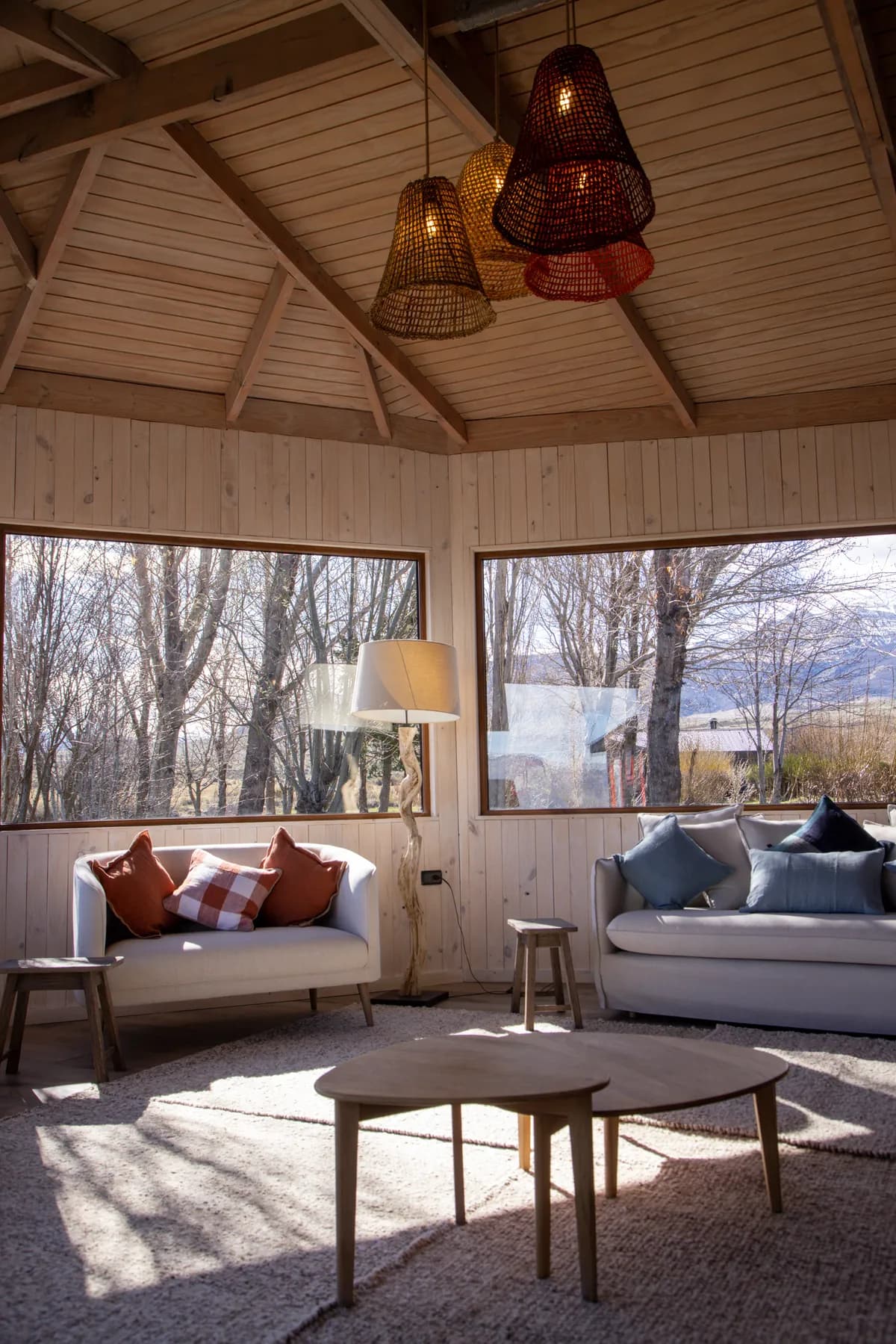 The lodge living room under its timber roof, with lamps and windows onto the trees