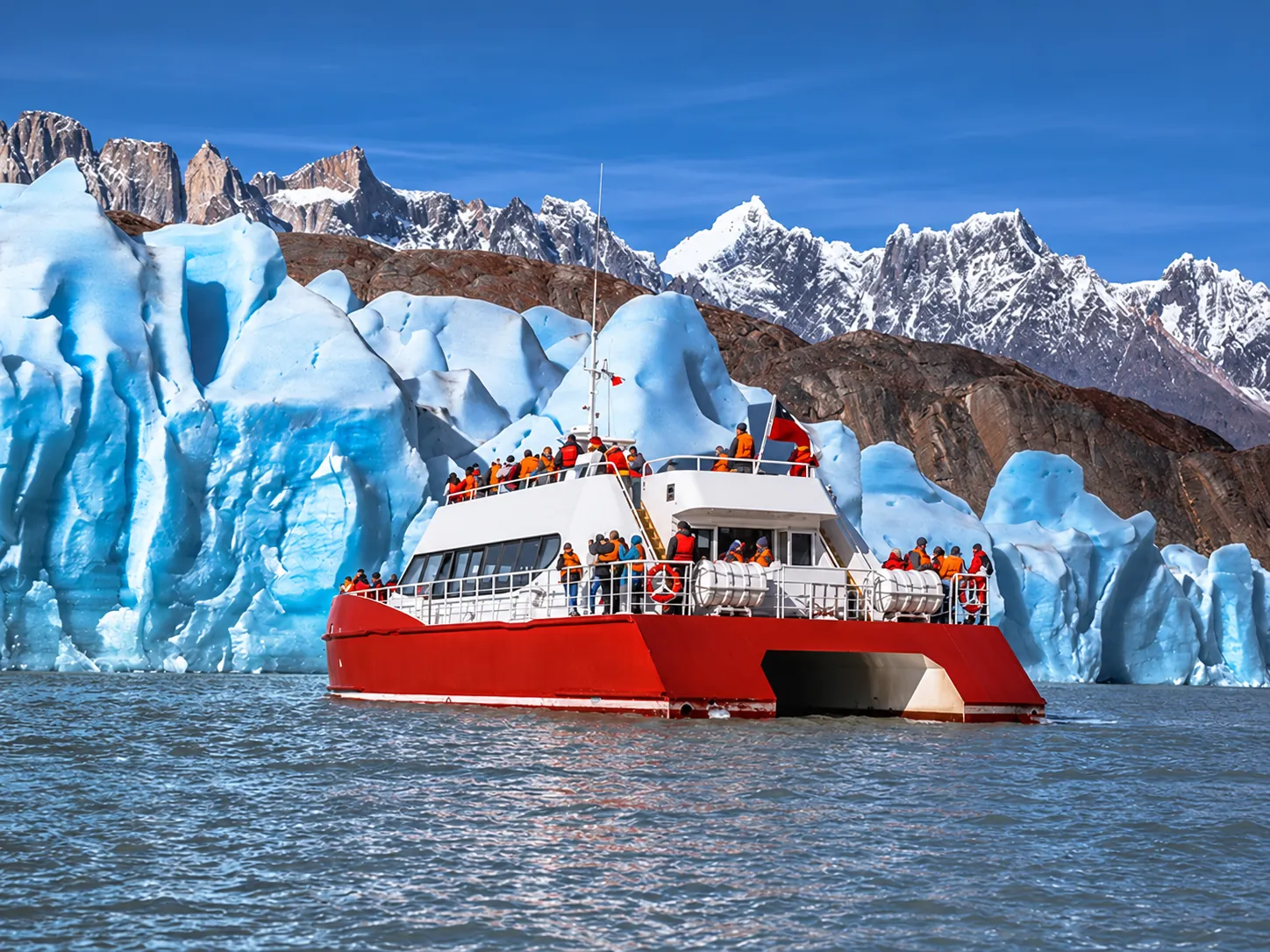 Red catamaran beside the blue ice of Grey Glacier